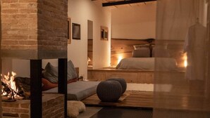 Um quarto acolhedor com lareira, uma cama, um banco e uma mesinha.