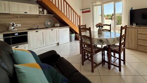 Una cucina moderna con mobili bianchi, una scala in legno, un'area pranzo con tavolo e sedie e una TV sulla destra.
