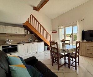 Eine moderne Küche mit weißen Schränken, einer Holztreppe, einem Essbereich mit Tisch und Stühlen sowie einem Fernseher auf der rechten Seite.