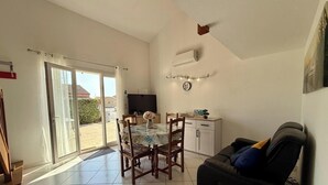 Un'ampia zona giorno con tavolo da pranzo, sedie, divano, televisore e una porta vetrata scorrevole che dà su un patio.