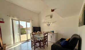 Ein geräumiger Wohnbereich mit Esstisch, Stühlen, einer Couch, einem Fernseher und einer Glastür, die auf eine Terrasse führt.