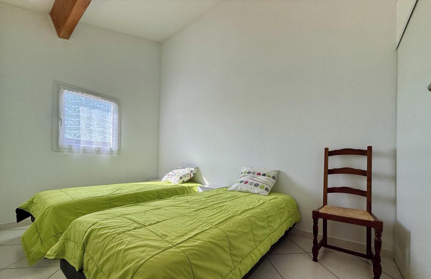 Quarto com duas camas, uma janela, uma cadeira e um vigário de madeira no teto.