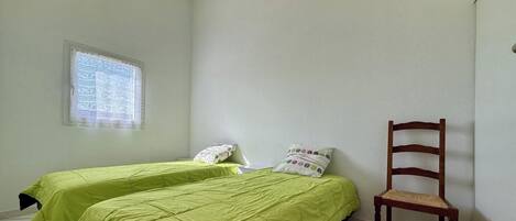 Quarto com duas camas, uma janela, uma cadeira e um vigário de madeira no teto.