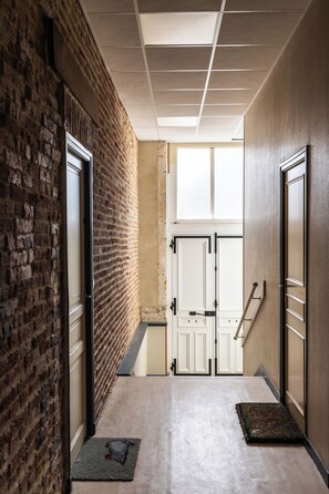A hallway with brick walls, a concrete floor, and a door leading to a room with a window. - TinyBeach, a seafront studio in Asnelles (Saint-Côme-de-Fresné)
