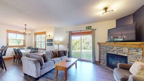 Een ruime woonkamer met een open haard, een eethoek met stoelen, en een grote televisie boven de open haard.