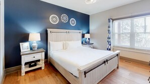 Een slaapkamer met een bed, nachtkastjes, decoratieve muurkunst, een raam met jaloezieën en een plafondlamp.