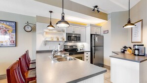 Une cuisine moderne dotée d’un îlot central, d’appareils électroménagers en acier inoxydable et de luminaires suspendus.