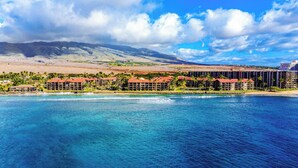 Un complejo turístico costero con varias edificaciones, una playa y montañas al fondo.