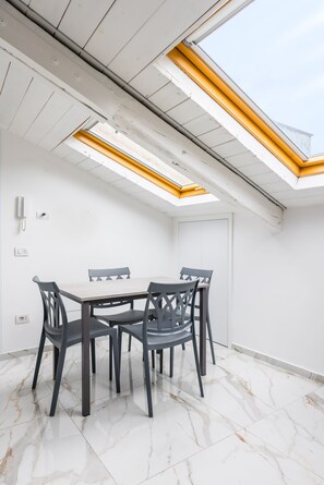 Ein Zimmer mit Dachfenster, einem Tisch mit Stühlen und einer weißen Tür.
