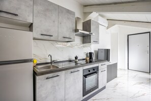 A modern kitchen with a marble countertop, stainless steel sink, and built-in oven. - Cozy Slooping Rooftop (Arenaccia)