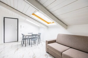 A room with a high ceiling, a skylight, a sofa, a dining table with chairs, and a door. - Cozy Slooping Rooftop (Arenaccia)