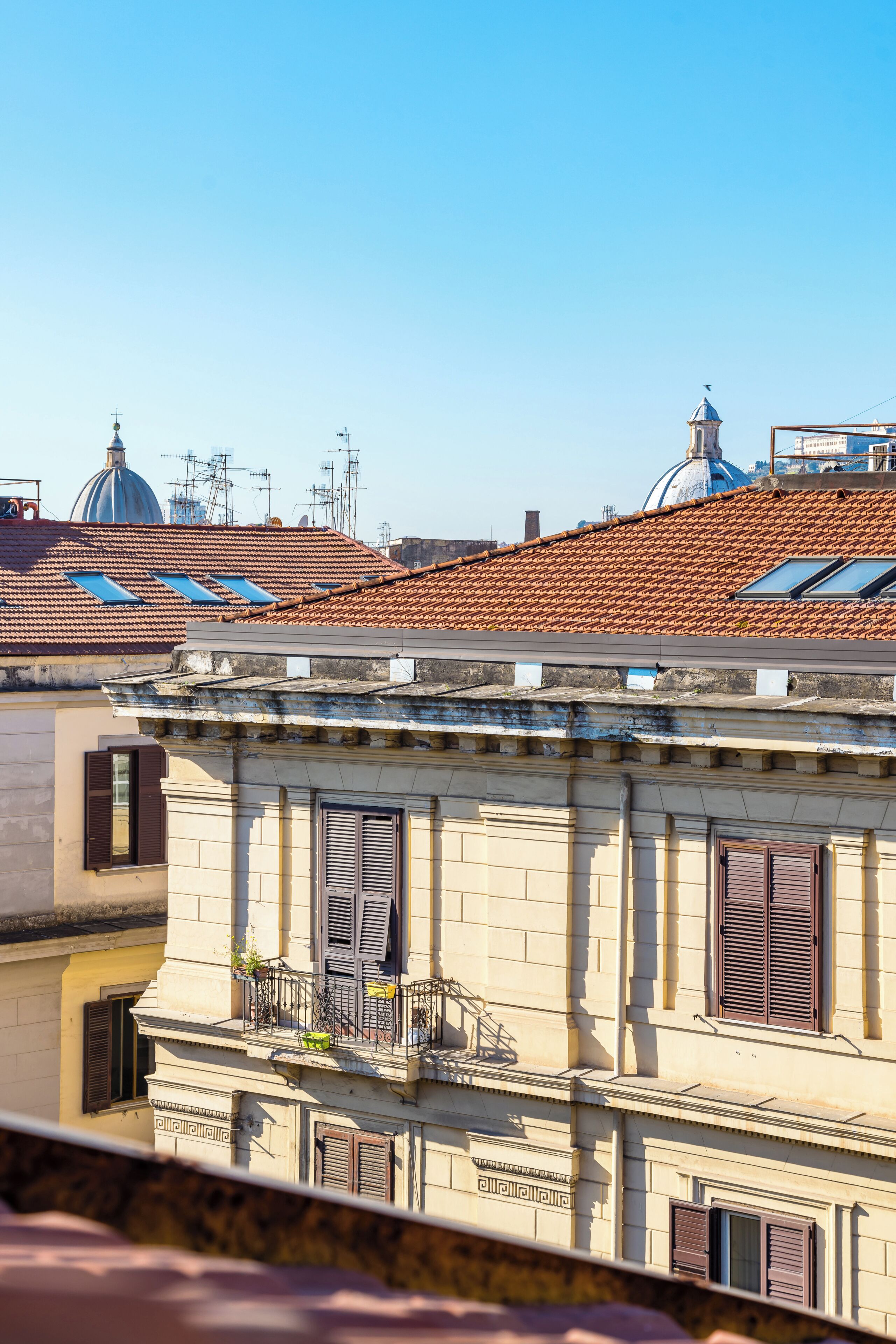 A building with a balcony, a window with shutters, and a dome structure in the background.