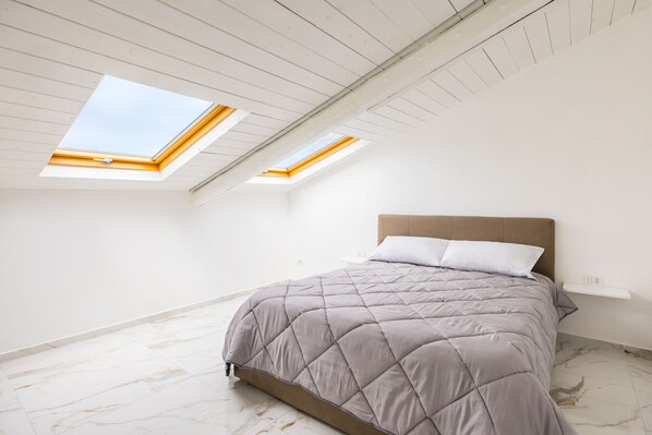 Ein Schlafzimmer mit Bett, Dachfenstern und Marmorboden.