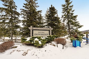 Un panneau indiquant « PASSAGE HISTORIQUE SUR NEIGE », entouré d’un paysage enneigé et d’arbres à feuilles persistantes.