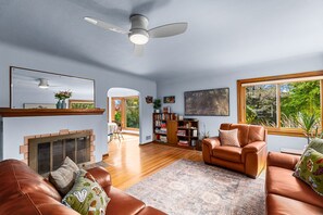 A living room with a fireplace, leather sofas, a bookshelf, and a large window with a view of greenery.
