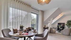 Ein modernes Wohnzimmer mit einem Essplatz, gedecktem Tisch für Tee, einer Couch und einem Fernseher im Hintergrund.