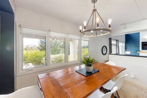 A dining area with a wooden table, white chairs, a potted plant, and a chandelier. - Bright Wintergreen Condo w/ Private Sauna & Golf (The Blue Mountains)