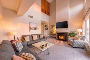 A living room with a sofa, coffee table, fireplace, TV, and a painting on the wall. - Relaxing Wintergreen Home | Golf/Mins to Blue (The Blue Mountains)