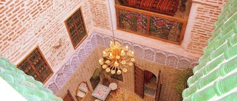 Een traditionele binnenplaats met een hangende kroonluchter, een behang met patroon en een bed met rode en groene beddengoed.