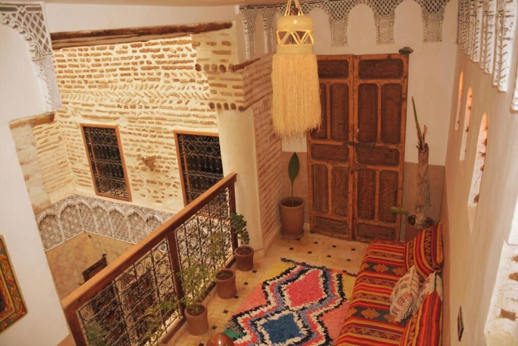 A traditional Moroccan interior with a wooden door, a hanging lamp, and a patterned rug.