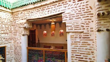 Una habitación con pared de ladrillo, ventana con celosías metálicas decorativas y techo de tejas verdes.