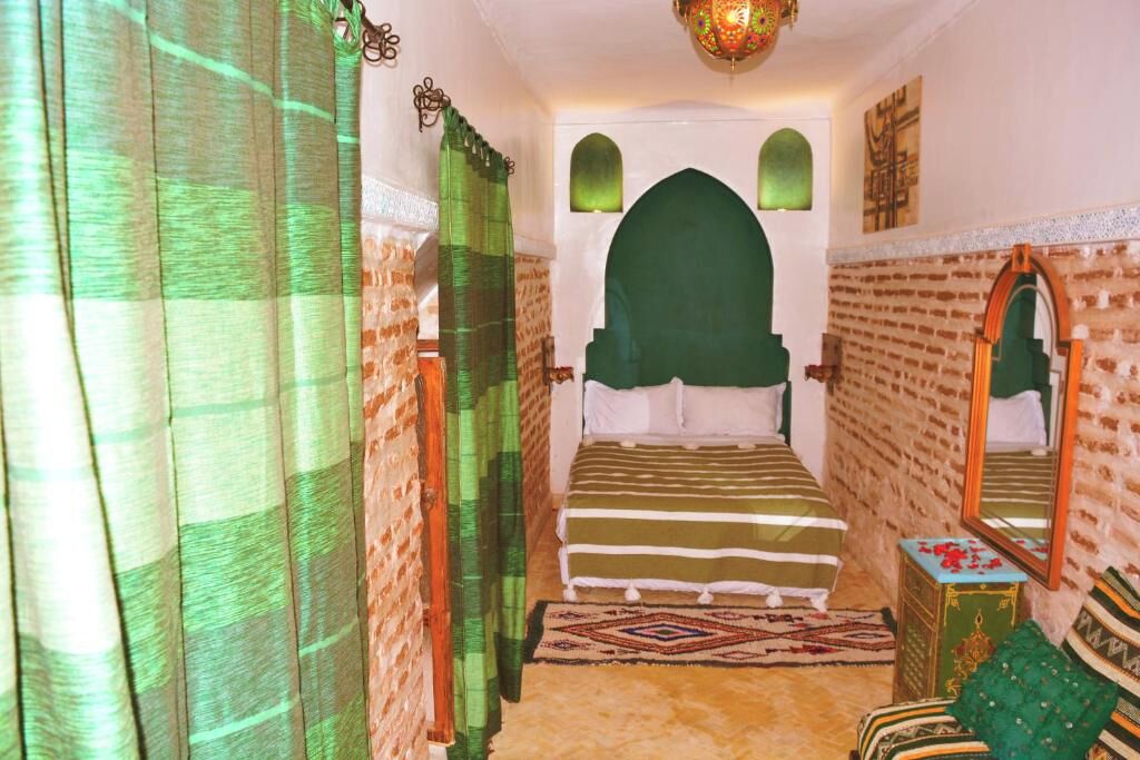 A room with a bed, a mirror, a small table, and a patterned rug.