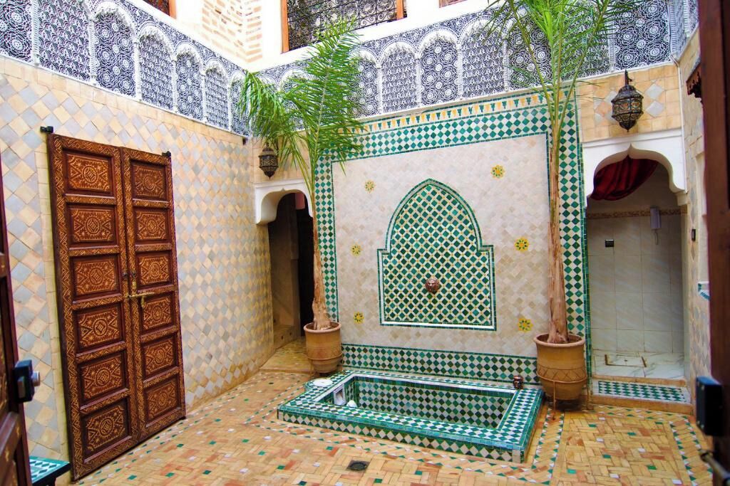 Ein Innenhof mit Fliesenboden, einer Holztür und einer Wand mit dekorativen geometrischen Mustern.