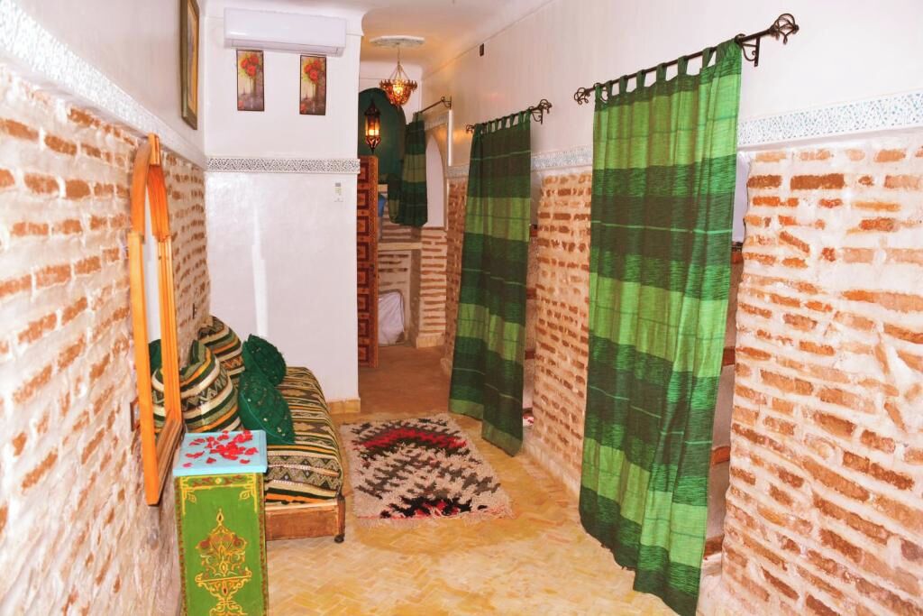Un pasillo estrecho con una pared de ladrillo, un tapete de diseño verde y blanco, un banco de madera y una cortina verde.