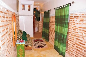 A narrow hallway with a brick wall, a green and white patterned rug, a wooden bench, and a green curtain. - Riad marrakech peace (Marrakech)