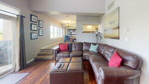 A spacious living room with a large sectional sofa, a dining area in the background, and a view through a large window. - Ground Floor Home, Steps to Blue Mtn Village (The Blue Mountains)