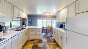 A kitchen with white cabinets, a dining area with a table and chairs, and a patterned floor. - Ground Floor Home, Steps to Blue Mtn Village (The Blue Mountains)