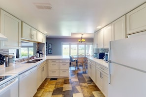 A kitchen with white cabinets, a dining area with a table and chairs, and a patterned floor. - Ground Floor Home, Steps to Blue Mtn Village (The Blue Mountains)