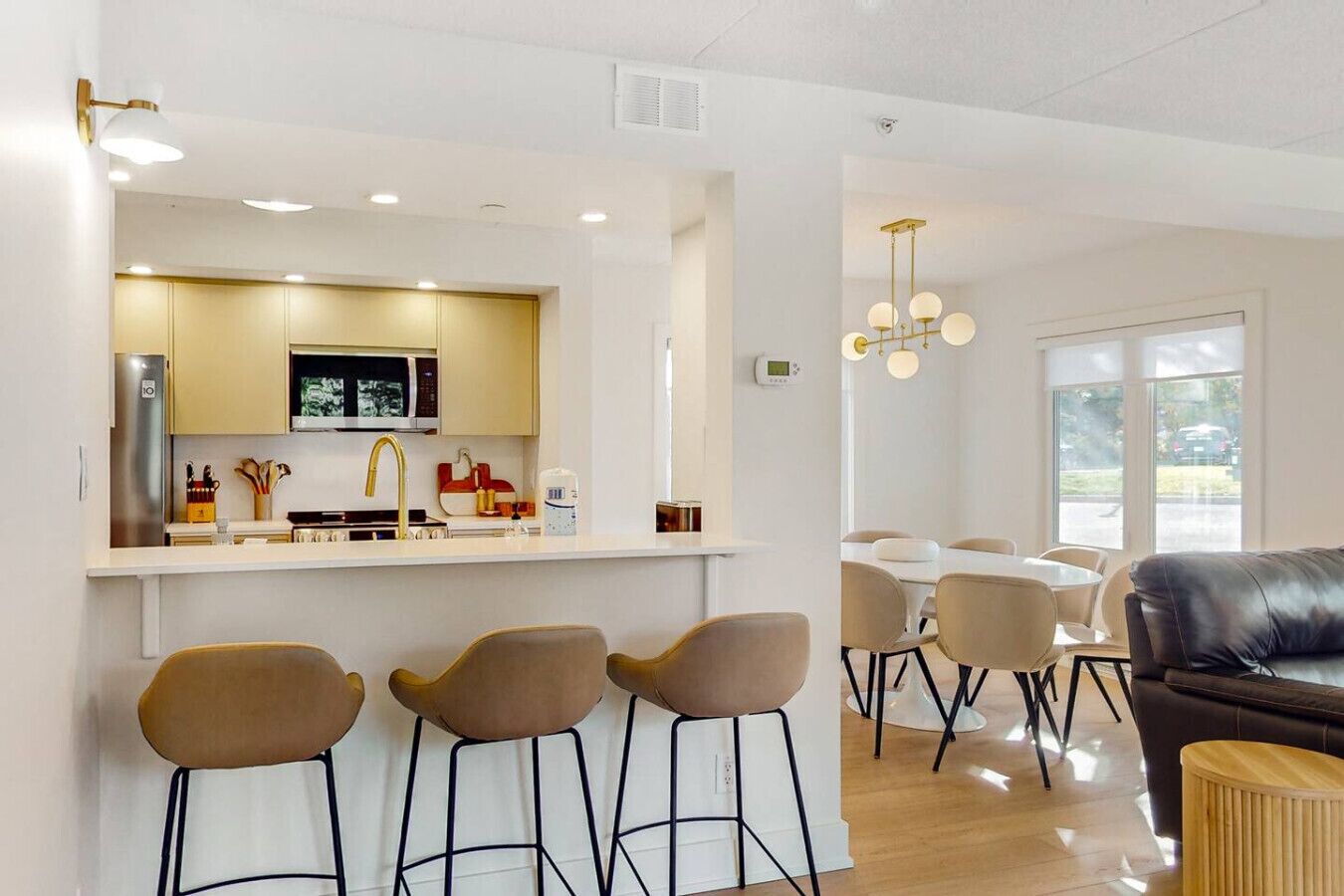 Una cocina moderna con una isla central, taburetes de bar, una zona de comedor con mesa y sillas, y un sofá de cuero.