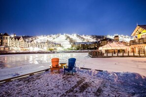 Hotel aan het water met een sneeuw bedekte veranda, twee stoelen en verlichte gebouwen op de achtergrond.