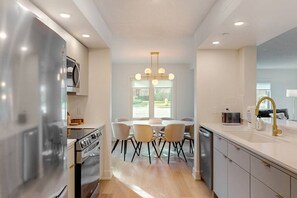 Een moderne keuken met een centraal eiland, roestvrijstalen apparatuur en een eethoek met een kroonluchter.