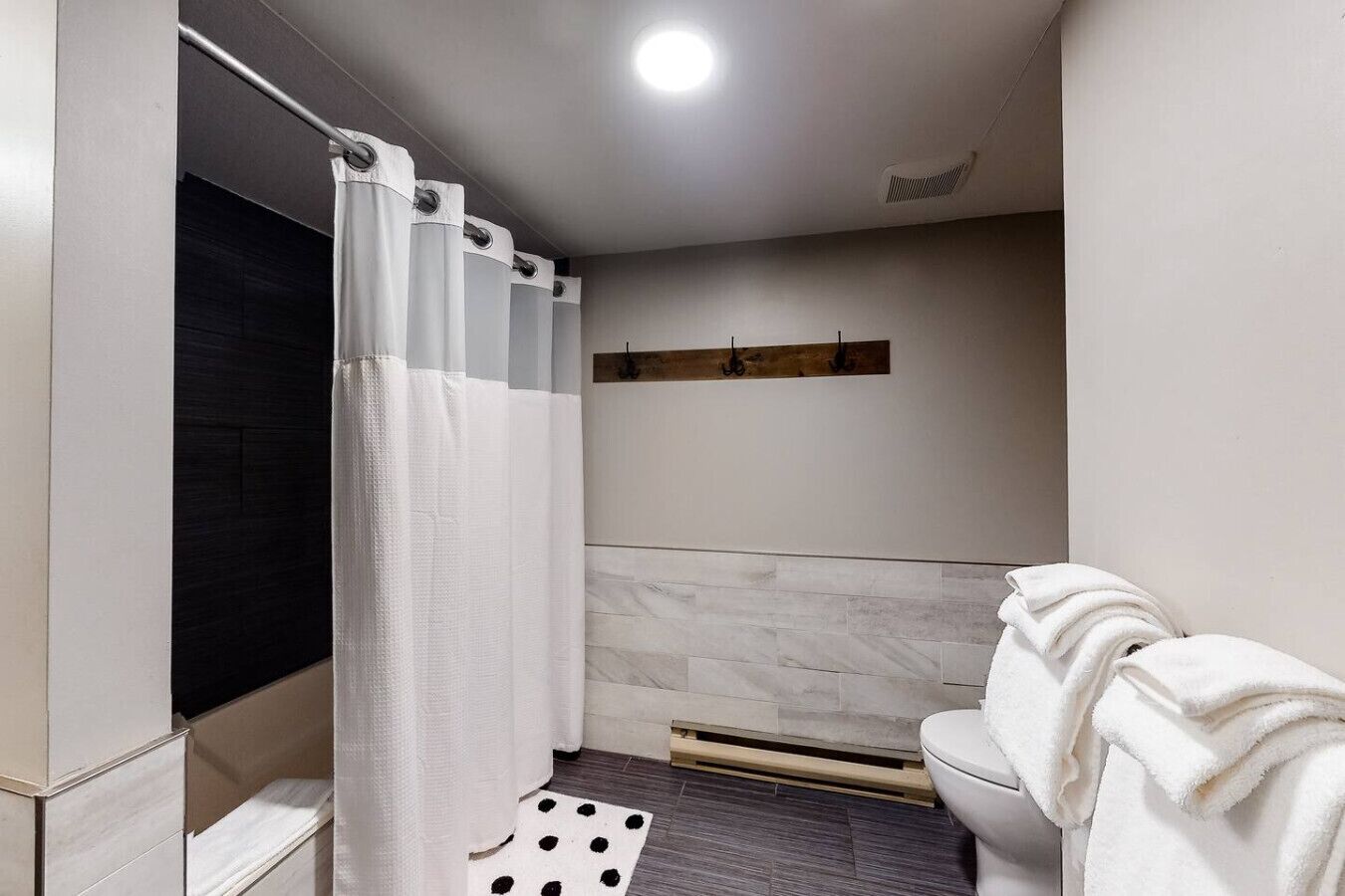 Un baño con cortina de ducha, inodoro, toallero y estante de madera.