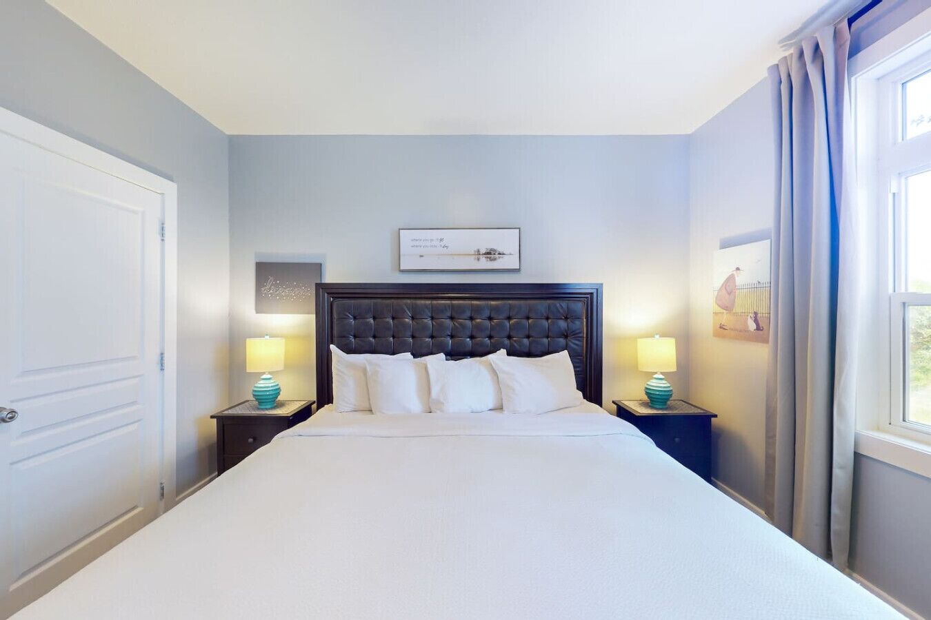 A hotel room with a large bed, two bedside tables with lamps, a framed picture on the wall, and a window with curtains.