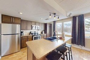 A modern kitchen with a stainless steel refrigerator, a microwave, an oven, and a sink. There are wooden cabinets, a countertop, and a window with curtains. - 3BDR Condo w/Private Sauna on Golf Course (The Blue Mountains)