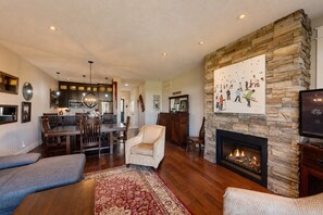 A living room with a fireplace, stone wall, and a dining area with wooden furniture. - The Links at Rivergrass: Pool/Village Access (The Blue Mountains)