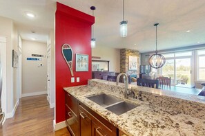A kitchen with granite countertops, stainless steel sinks, and a red accent wall. - The Links at Rivergrass: Pool/Village Access (The Blue Mountains)