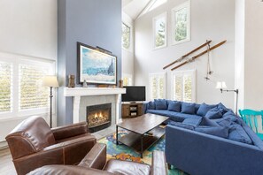 Een woonkamer met een open haard, een grote blauwe modulaire bank, een bruine leren bank en een televisie.