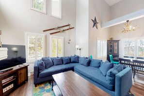 Ein Wohnzimmer mit Ecksofa, Flachbildfernseher, Couchtisch aus Holz und Bücherregal.