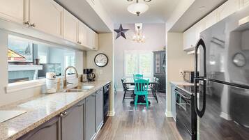 A modern kitchen with a central island, a dining area with teal chairs, and a large window.