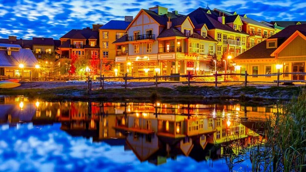 A waterfront property with multiple buildings, a reflective water body, and a clear sky. - Renovated 3BDR Family Condo | Slope-Side at Blue! (The Blue Mountains)