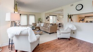 A living room with a sofa, armchair, and coffee table, a dining area with chairs, and a kitchen area with a stove. - Cozy & Chic Mountain Getaway | Steps to BM Village (The Blue Mountains)