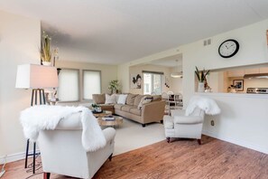 Ein Wohnzimmer mit Sofa, Sessel und Couchtisch, ein Essbereich mit Stühlen und eine Küchenzeile mit Herd.