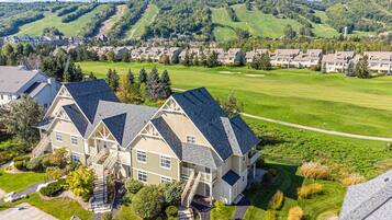 A large, multi-story house with a steep roof, surrounded by a well-maintained lawn and a golf course in the background.
