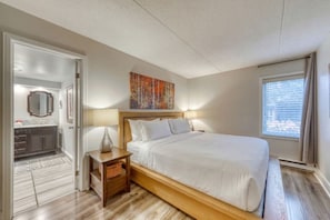 Une chambre d’hôtel équipée d’un lit, d’une table de chevet, d’une lampe, d’œuvres d’art et offrant une vue sur la ville par une fenêtre.