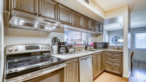 A kitchen with a stove, microwave, and dishwasher, wooden cabinets, and a window. - Heart of the Village Ground-Floor Condo for 7 (The Blue Mountains)