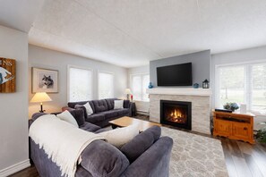 A modern living room with a fireplace, a sofa set, a flat-screen TV, and a mounted artwork. - 3BDR Mountain Side Retreat, Steps to the Village (The Blue Mountains)